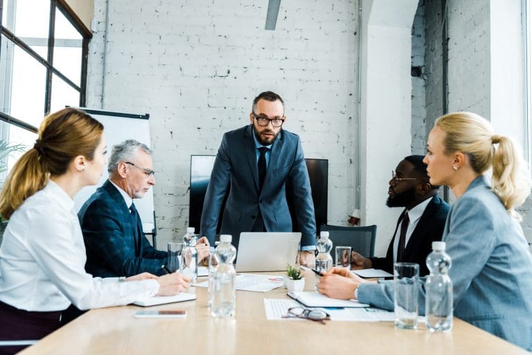 handsome business coach standing near multicultural businessmen and businesswomen